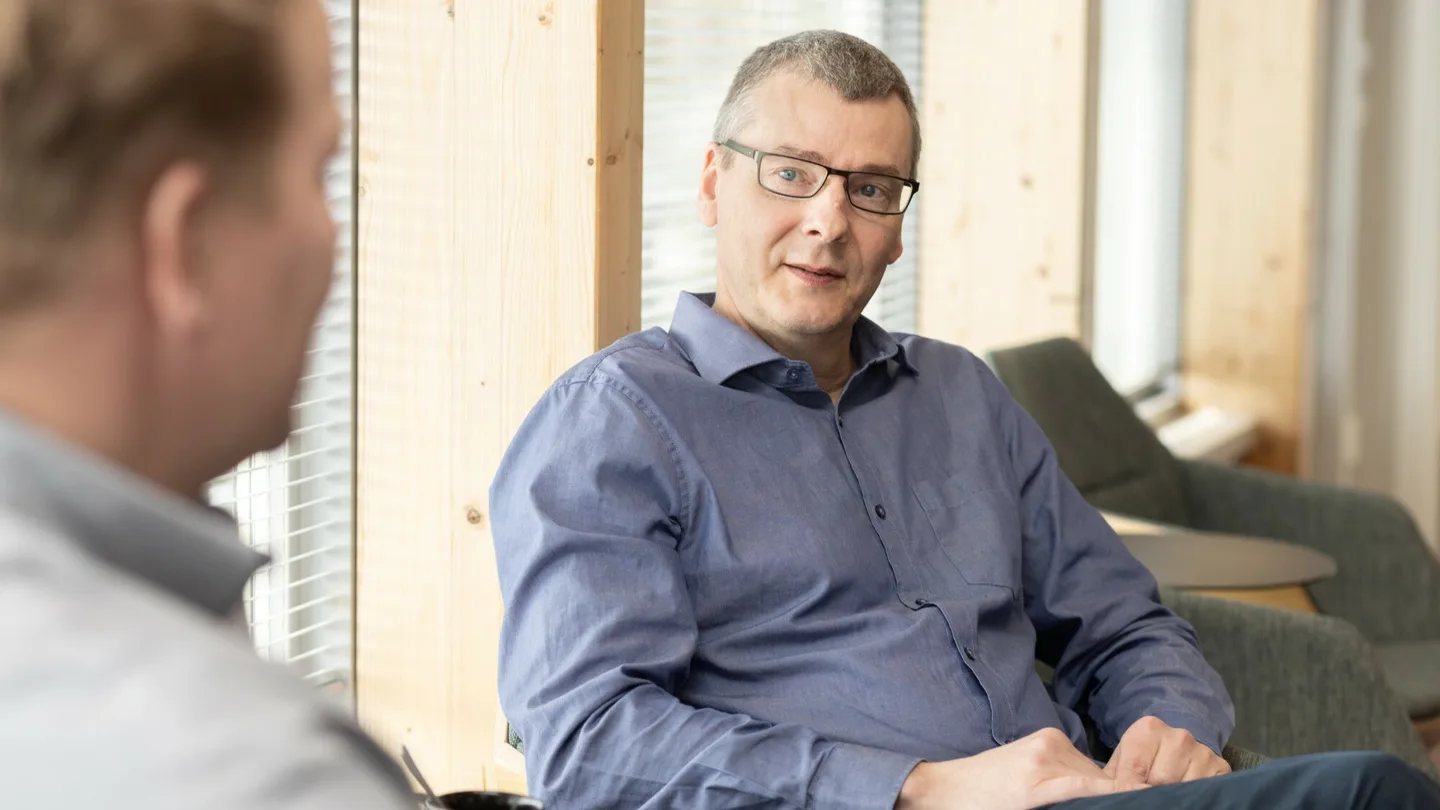 Investoinnit silmalasipainen mies istuu ja kuuntelee henkiloa jonka paa nakyy kuvassa vasemmalla