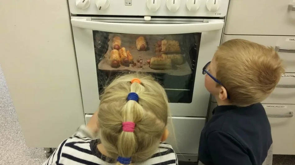 tyttö ja poika lattialla istumassa vahtimassa uunissa kypsyviä nakkikääröjä