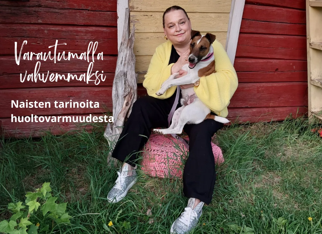 Hymyilevä Mervi Mäki-Neste istuu punamultaisen rakennuksen edessä pieni koira sylissään