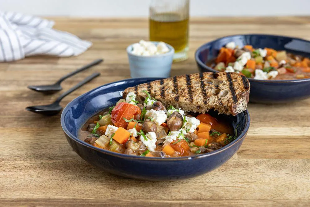 kaksi lautasellista papukasvissoppaa, koristeltu valkoisella juustonokareilla ja raidlliseksi grillatuilla leipäviipaleilla