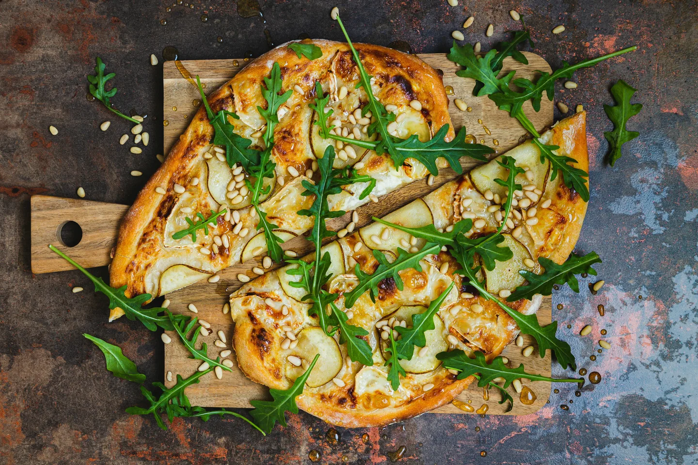 Päärynällä, vuohenjuustolla, rucolalla ja pinjansiemenillä päällystetty puolitettu pizza puisella leikkuulaudalla