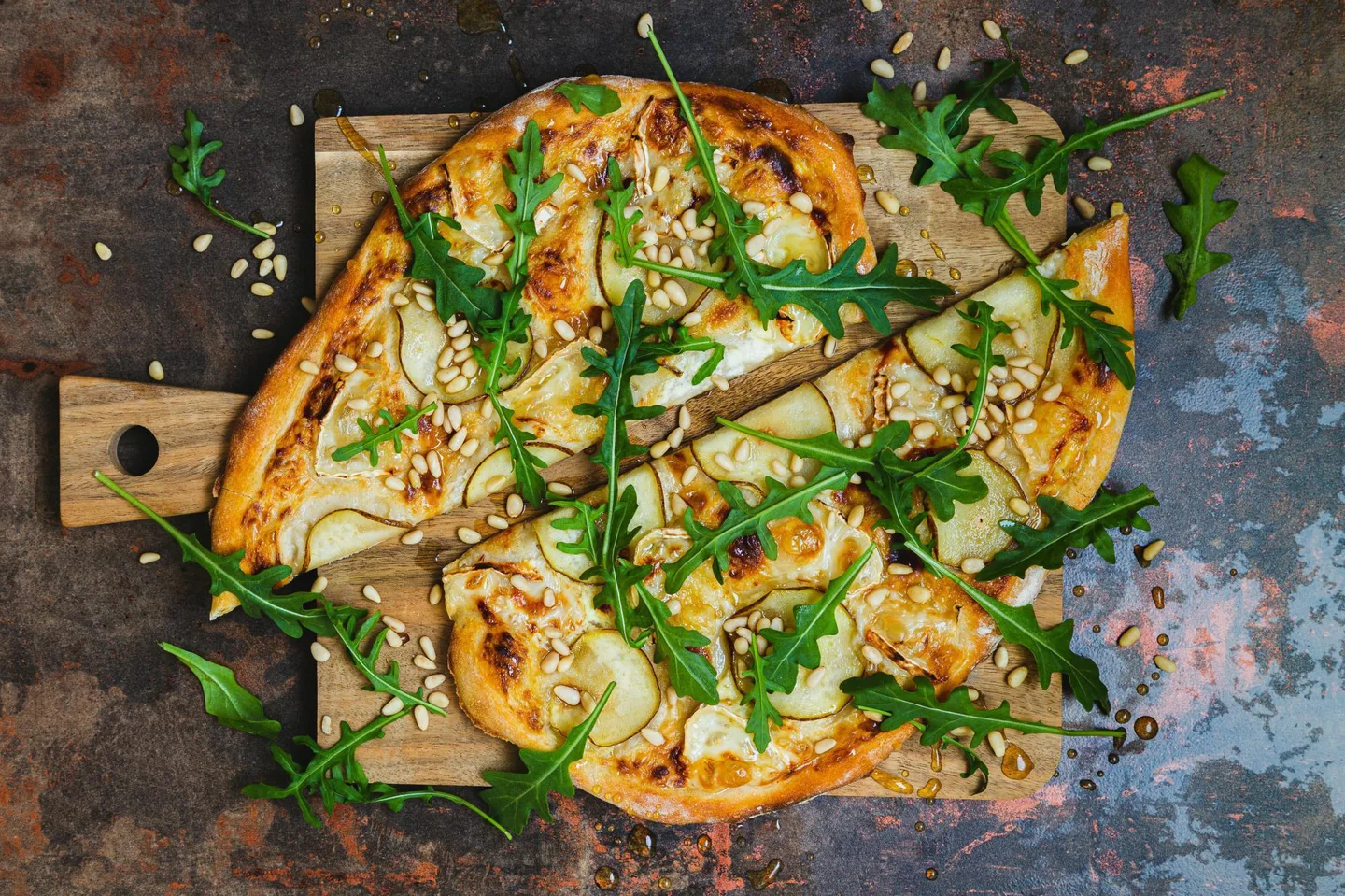 Päärynällä, vuohenjuustolla, rucolalla ja pinjansiemenillä päällystetty puolitettu pizza puisella leikkuulaudalla