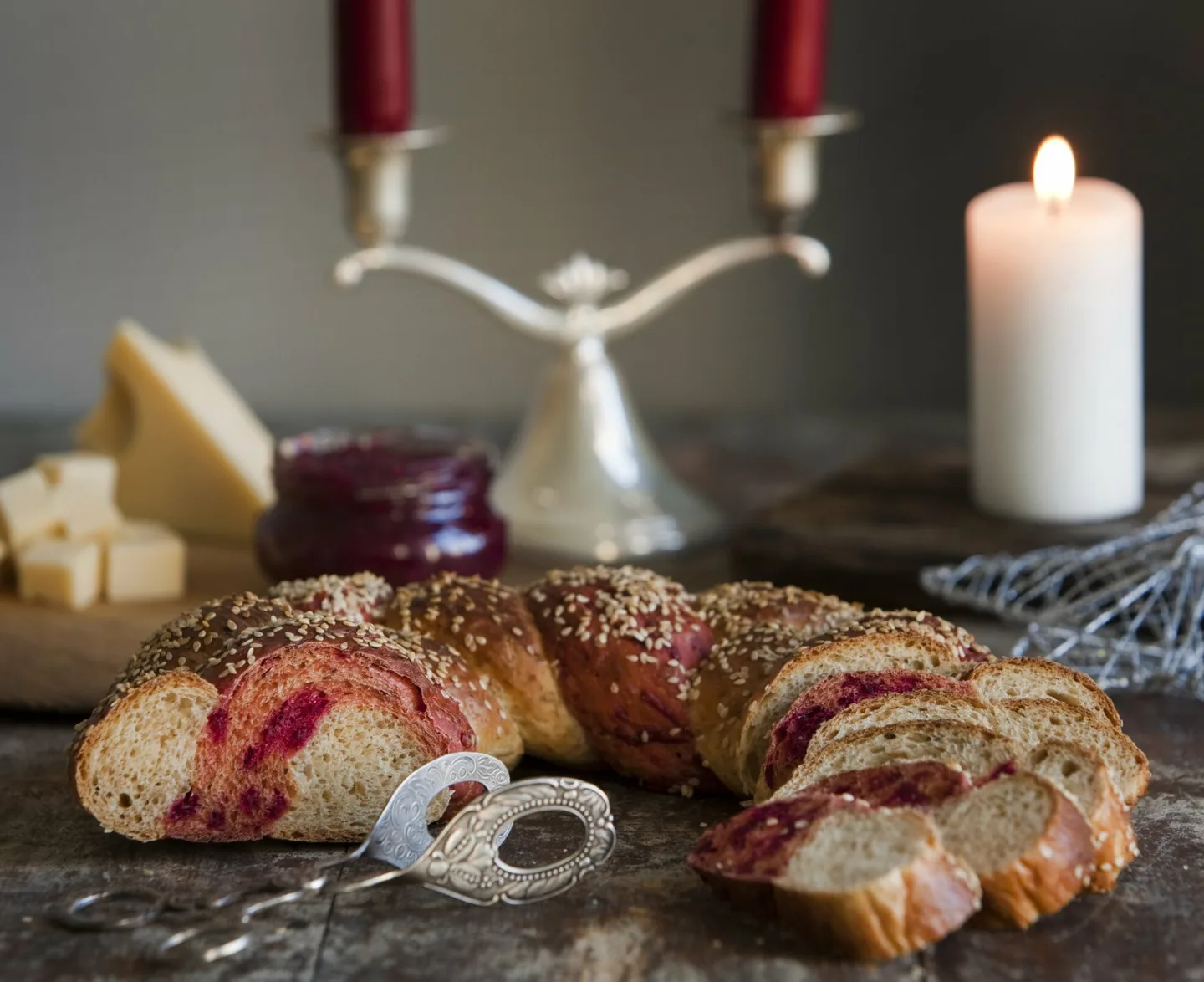 Osittain punajuurella värjättyä ja viipaloitua leipäkranssia tarjoiluvadilla, taustalla juustoa, hilloa ja kynttilöitä