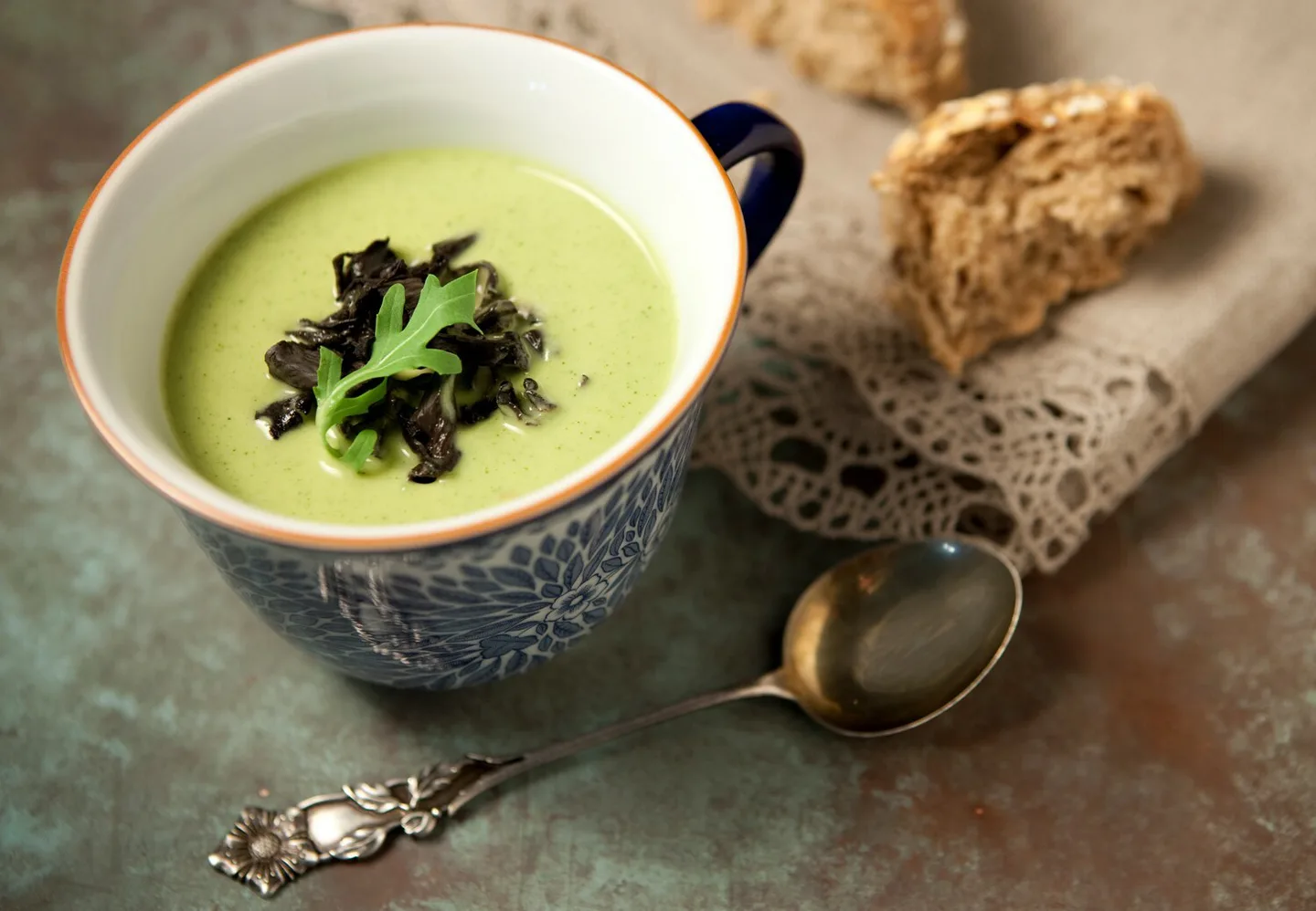 Vihreää sosekeittoa kupissa, sämpylää taustalla