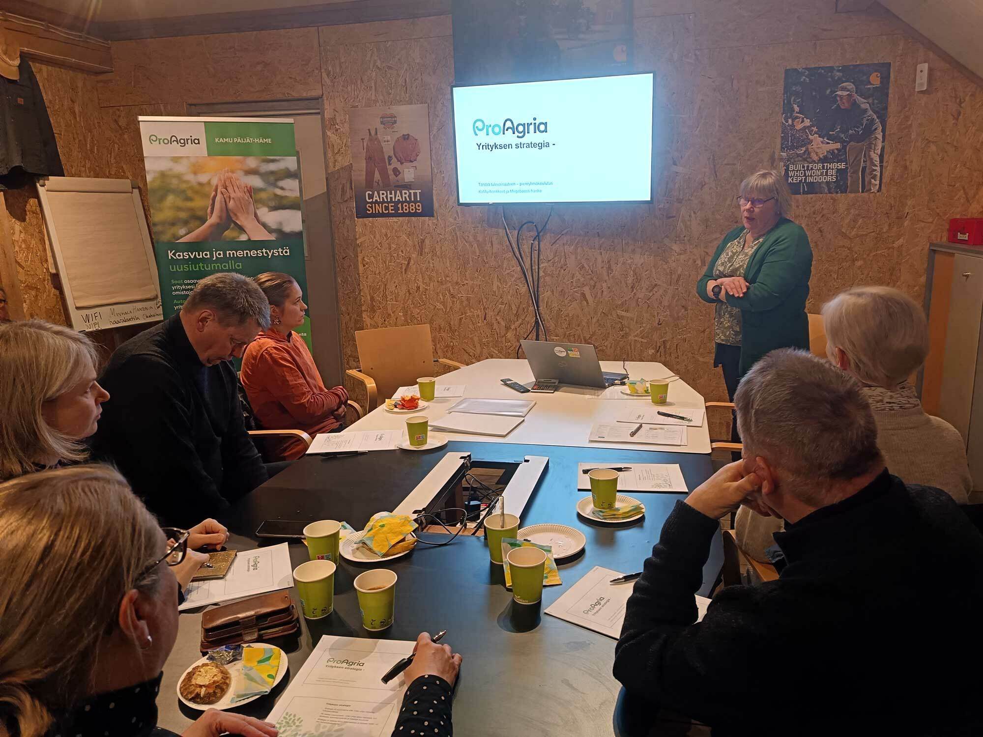 Ihmisiä pöydän äärellä kuuntelemassa luentoa