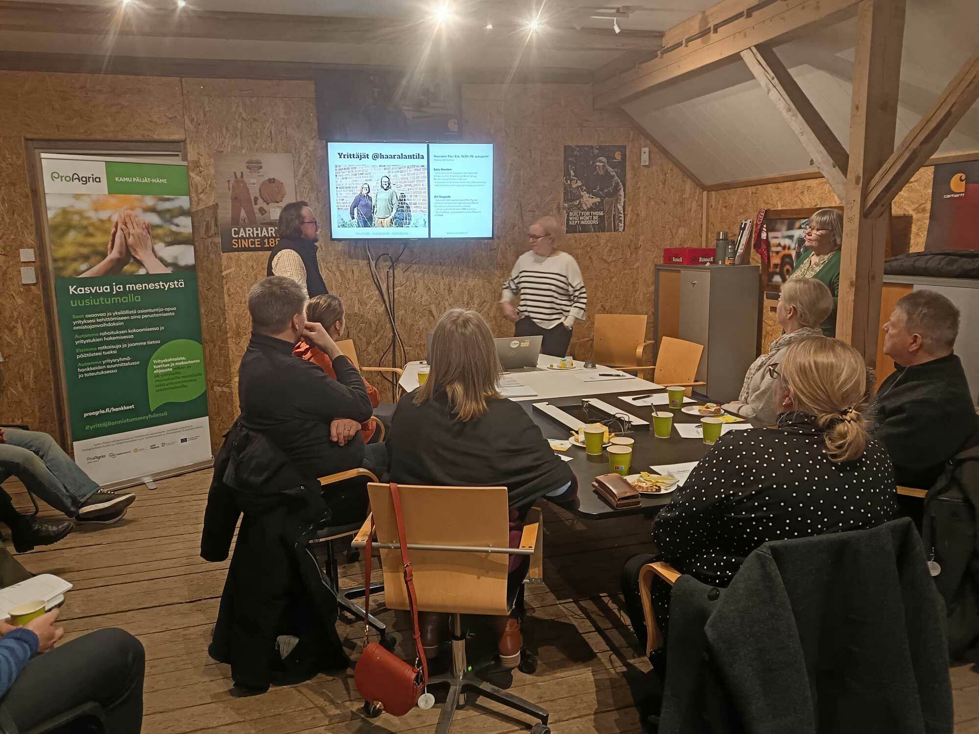 Kaksi ihmistä puhuu pöydän edessä ryhmälle