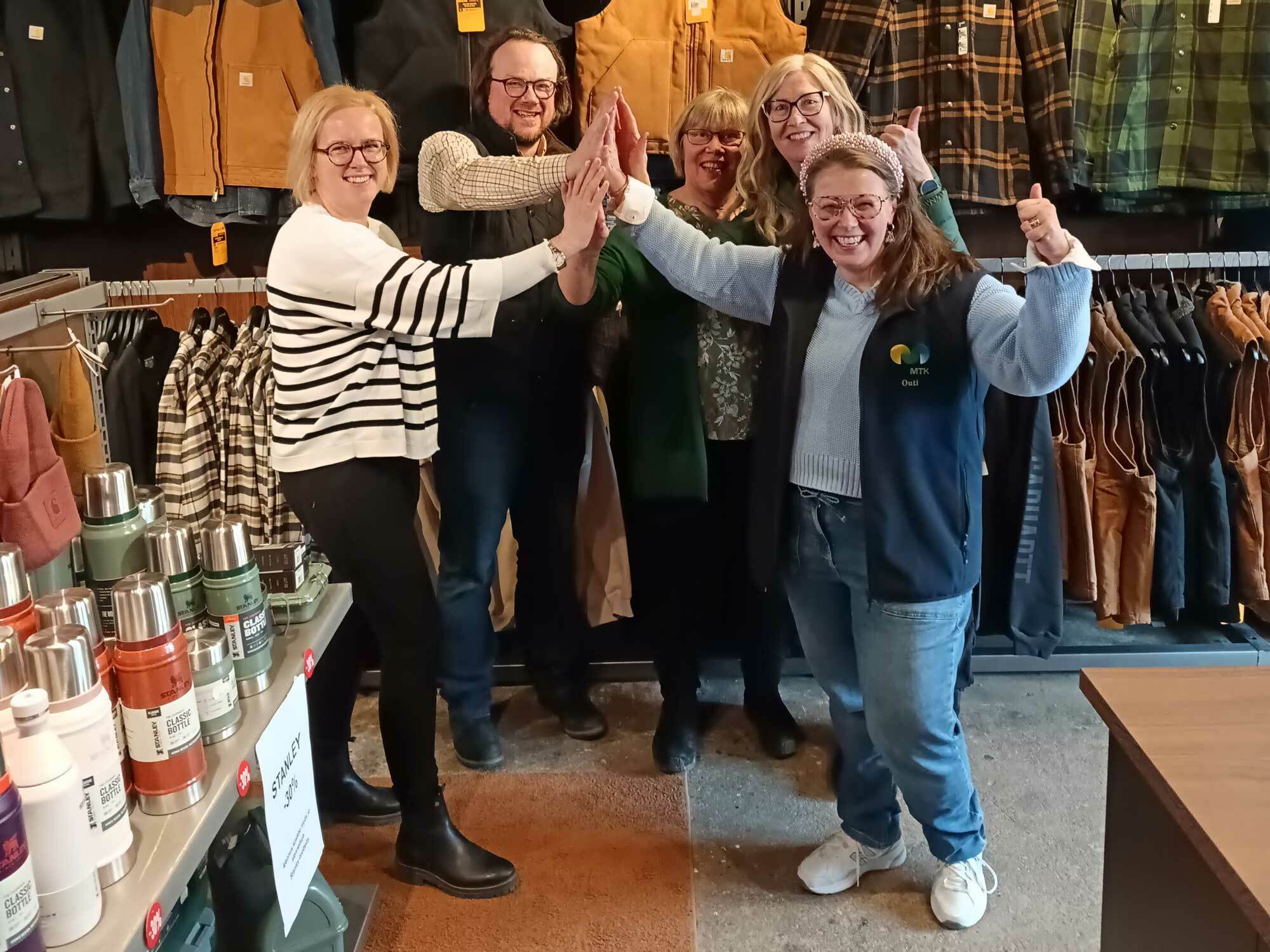 Viisi ihmistä lyö iloisina kädet yhteen myymälässä