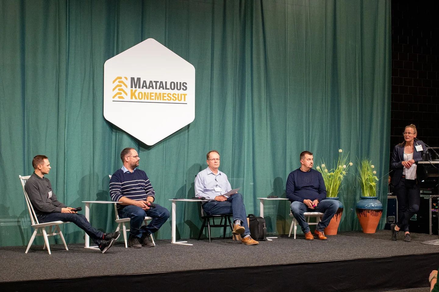 Lavalla keskustelijat ja juontaja, Maatalouskonemessut-kyltti taustalla.