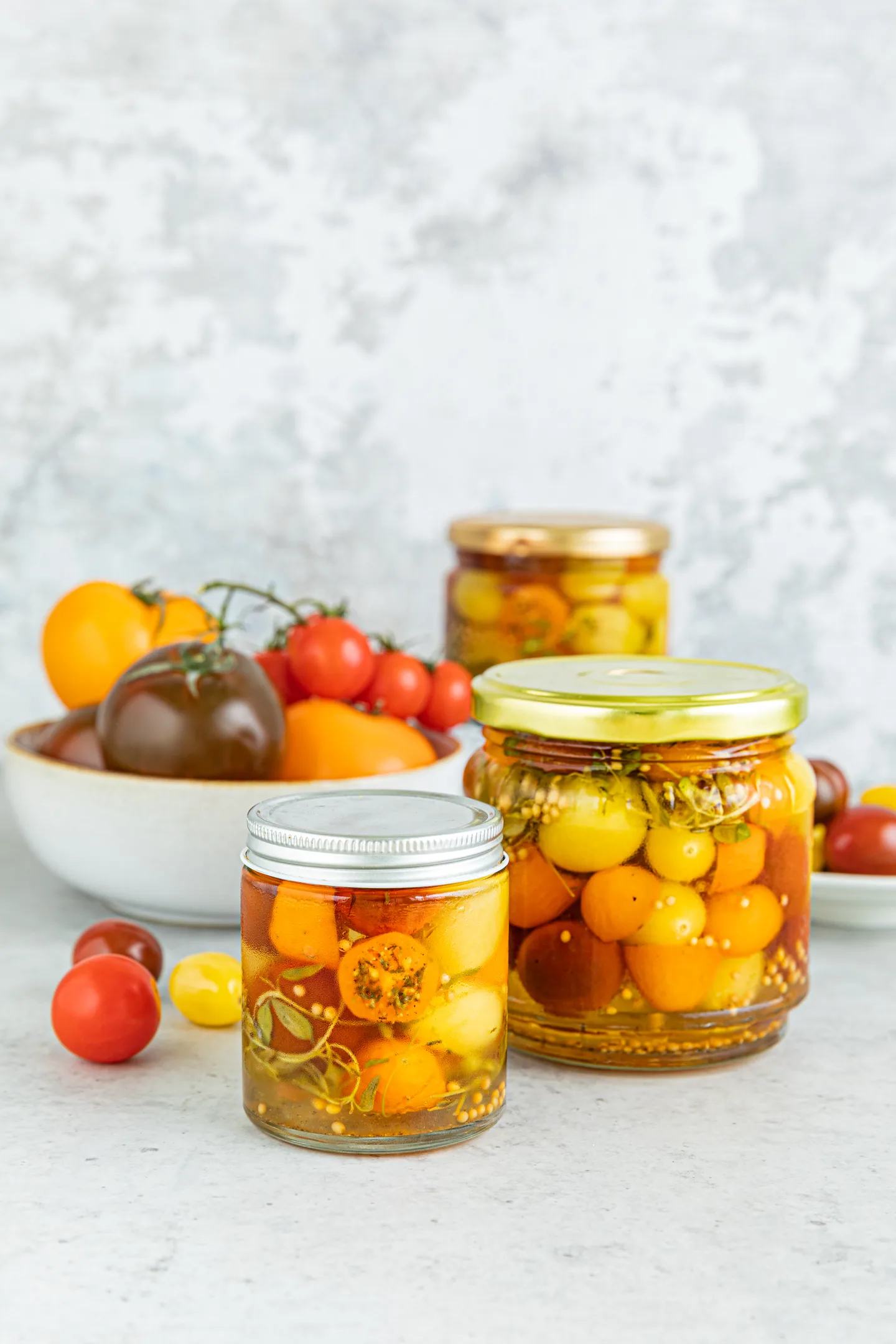 Kolme purkillista valkosipuli-timjamitomaatteja ja kulhossa tomaatteja